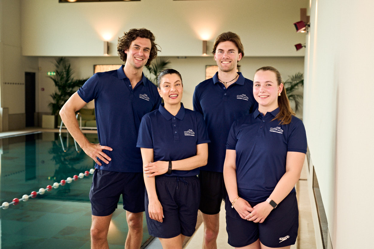 Four TSA coaches in navy team polos stand together beside the pool
