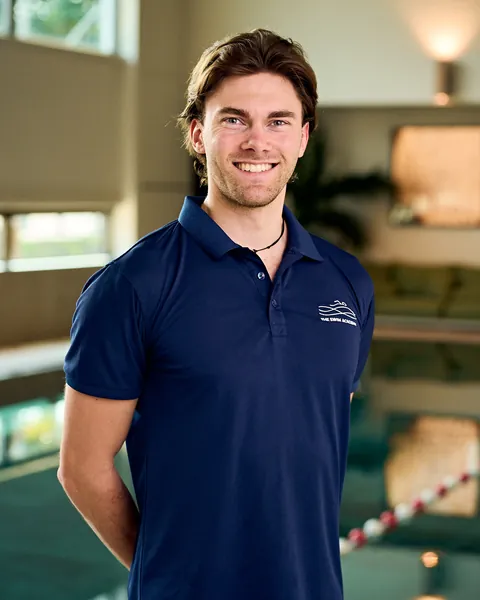 Julian, TSA coach, smiling beside the pool in a navy TSA polo