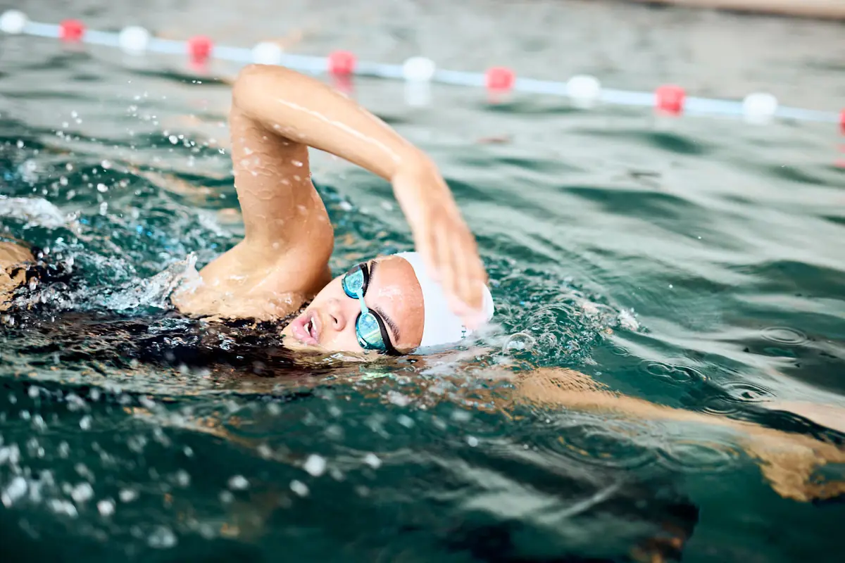 A swimmer in goggles turns to breathe during freestyle, arm recovering above the water