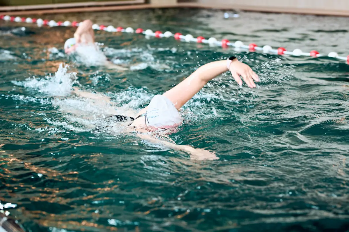 A swimmer in a TSA cap swims freestyle along the lane rope