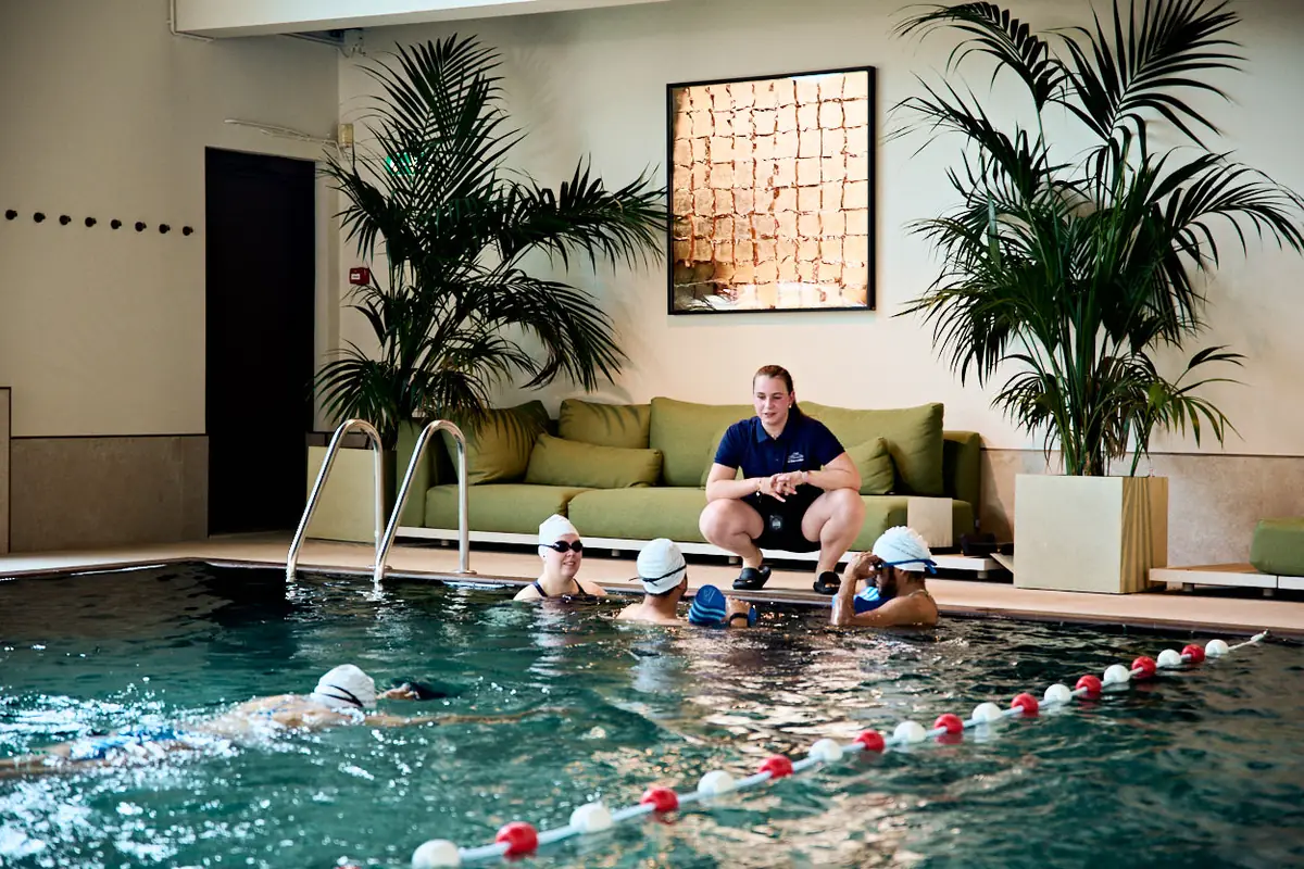 A coach crouches poolside, guiding a small group of swimmers at the wall at Special Sports