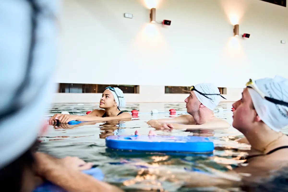 Swimmers with kickboards listen to their coach during a small-group lesson