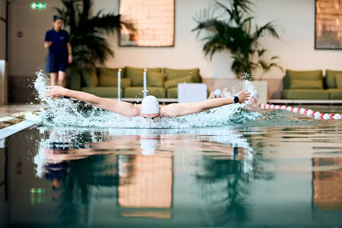 A swimmer trains butterfly while a coach watches from the poolside